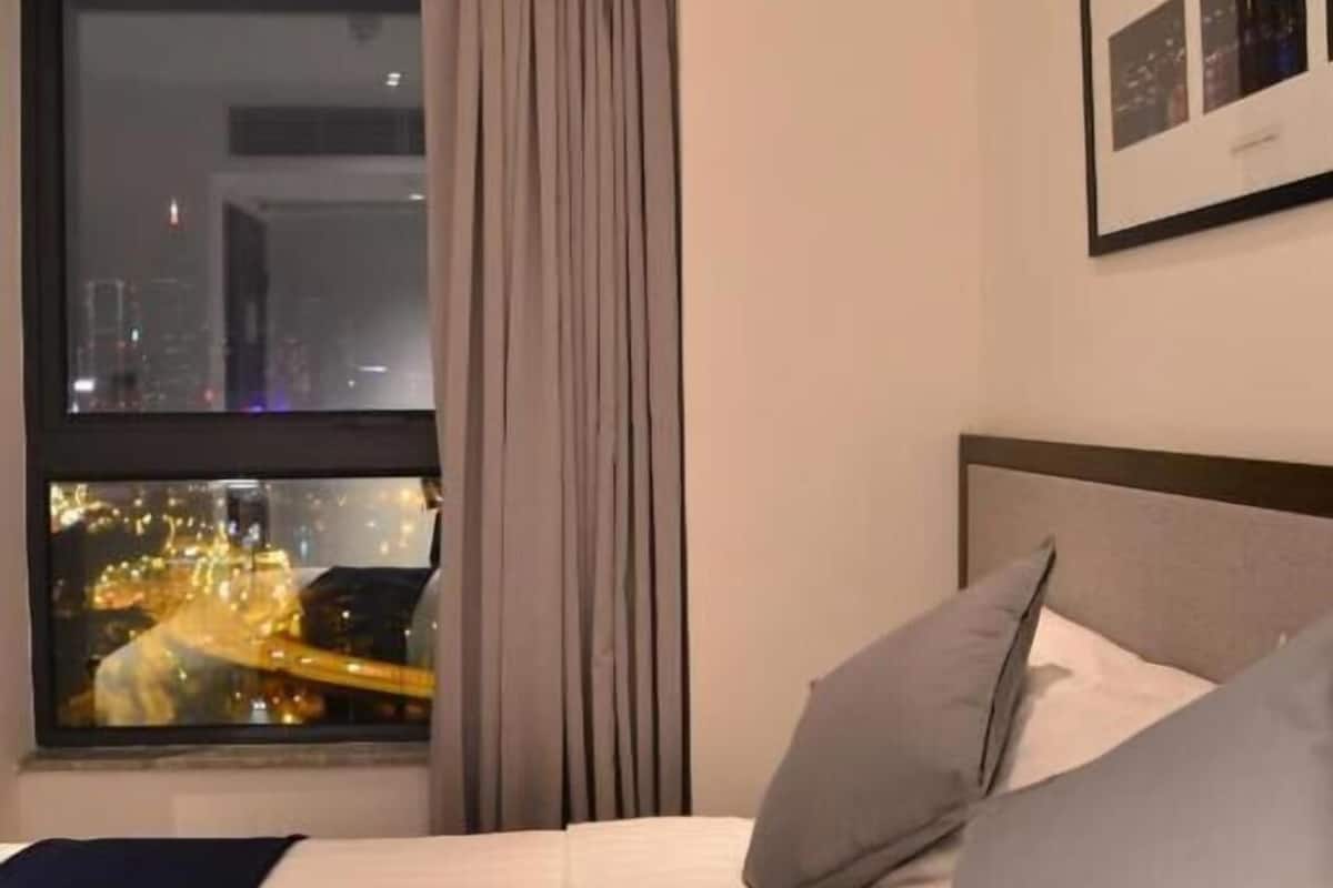 A hotel room with a bed, a window with curtains, a framed picture on the wall, and a cityscape view.