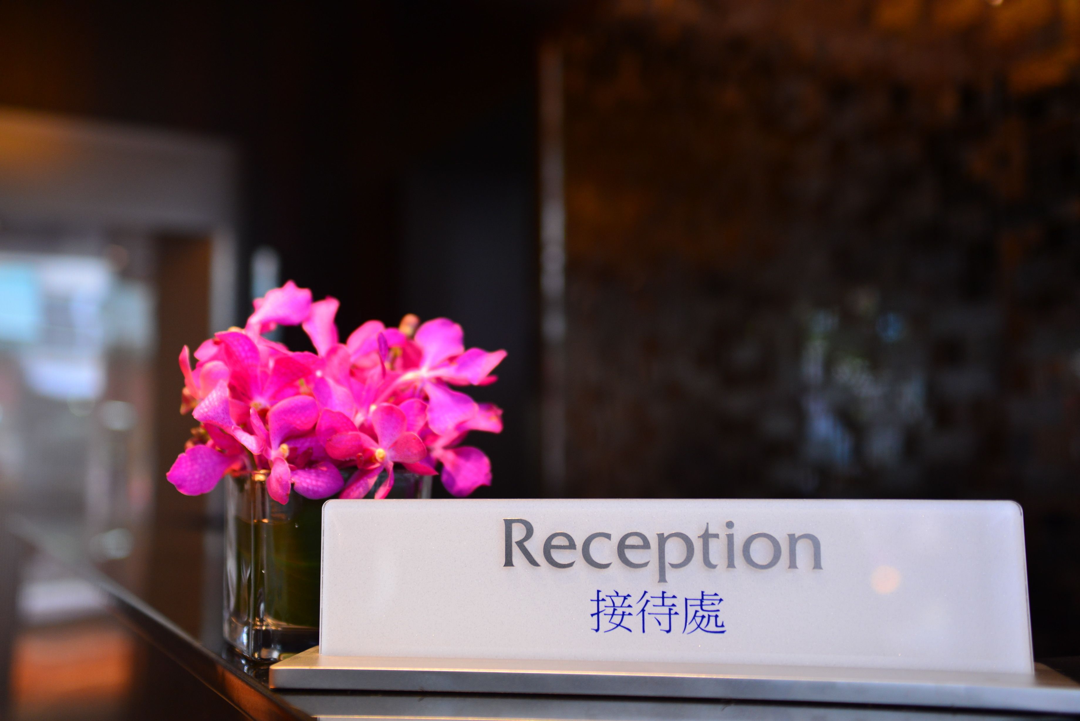 Un mostrador de recepción con un letrero que dice 'Reception' y un florero de flores rosadas.