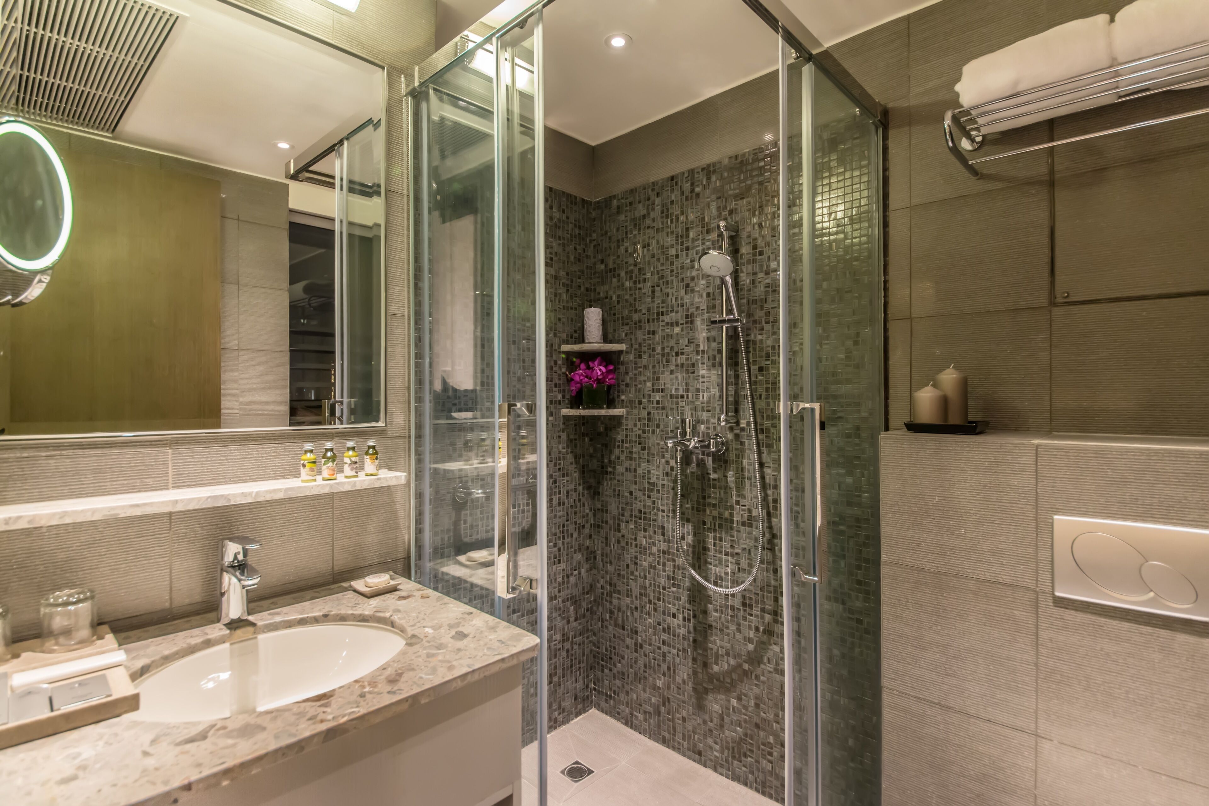 Un baño moderno con ducha de vidrio, un espejo grande y encimera de mármol.