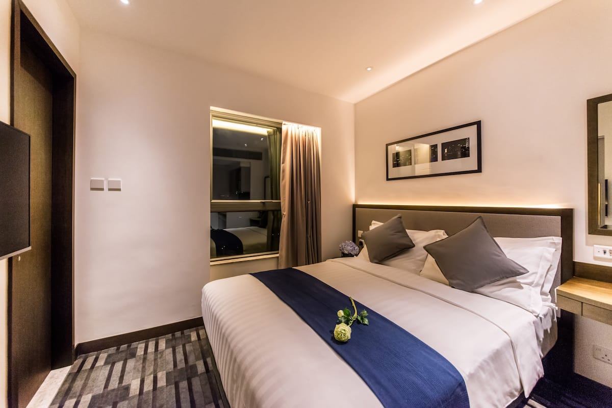 A hotel room with a large bed, a window with curtains, a bedside table with a lamp, and a wall-mounted TV.