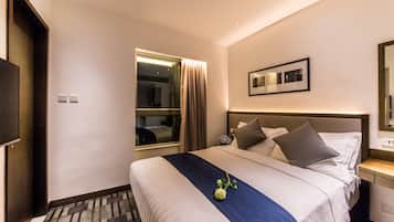 Habitació d'hotel amb un llit gran, una finestra amb cortines, una taula de nit amb una làmpada i un televisor fixat a la paret.