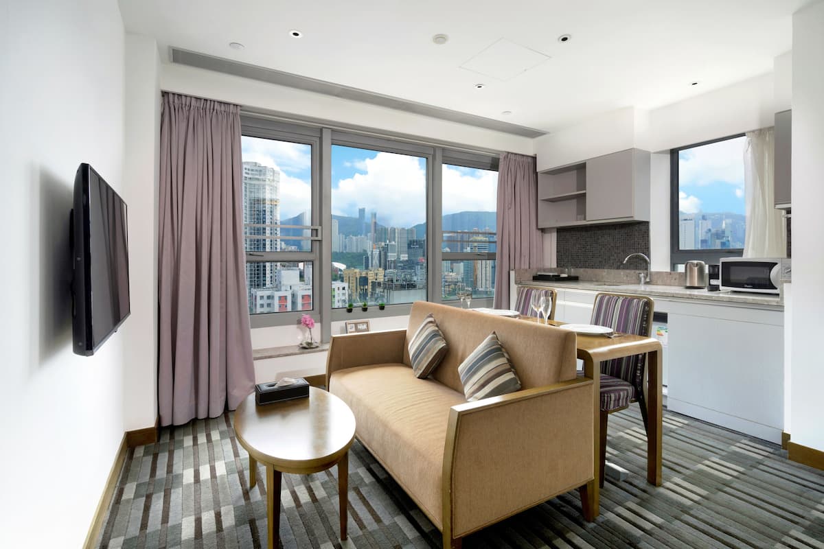A modern hotel room with a sofa, dining table, and kitchen area.