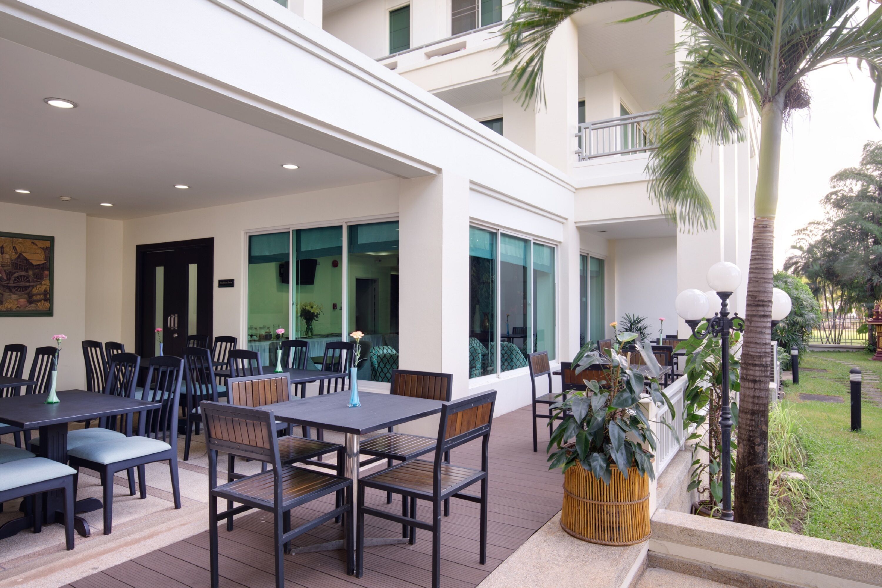 Un espace extérieur aménagé pour les repas, avec des tables et des chaises, un balcon doté d’une balustrade et un palmier.