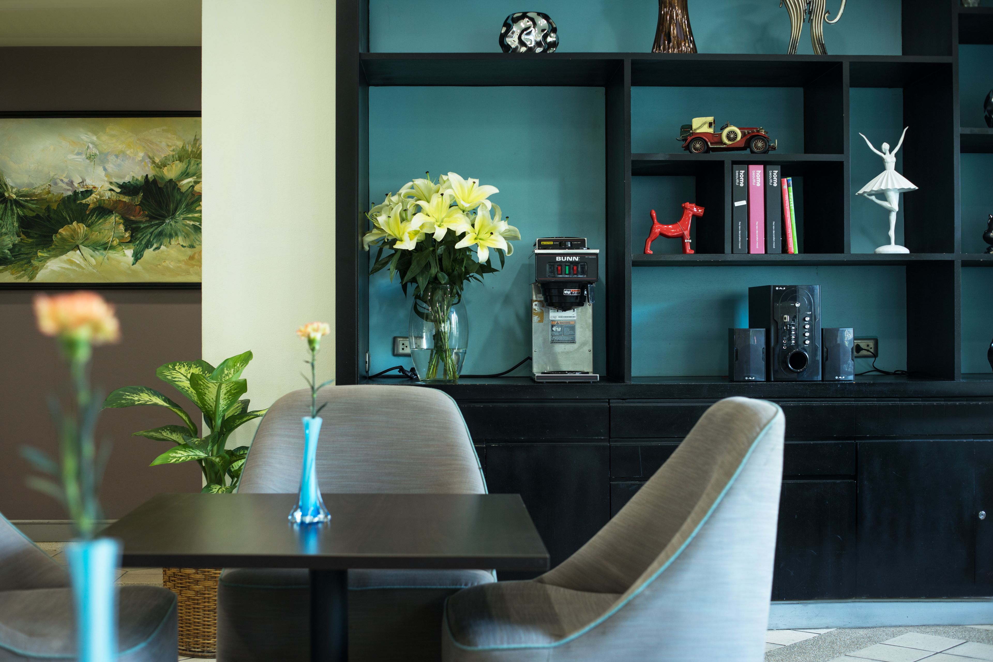 Una sala de estar moderna con una estantería azul oscuro, una cafetera y un jarrón con flores amarillas.