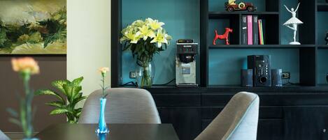 Una sala de estar moderna con una estantería azul oscuro, una cafetera y un jarrón con flores amarillas.
