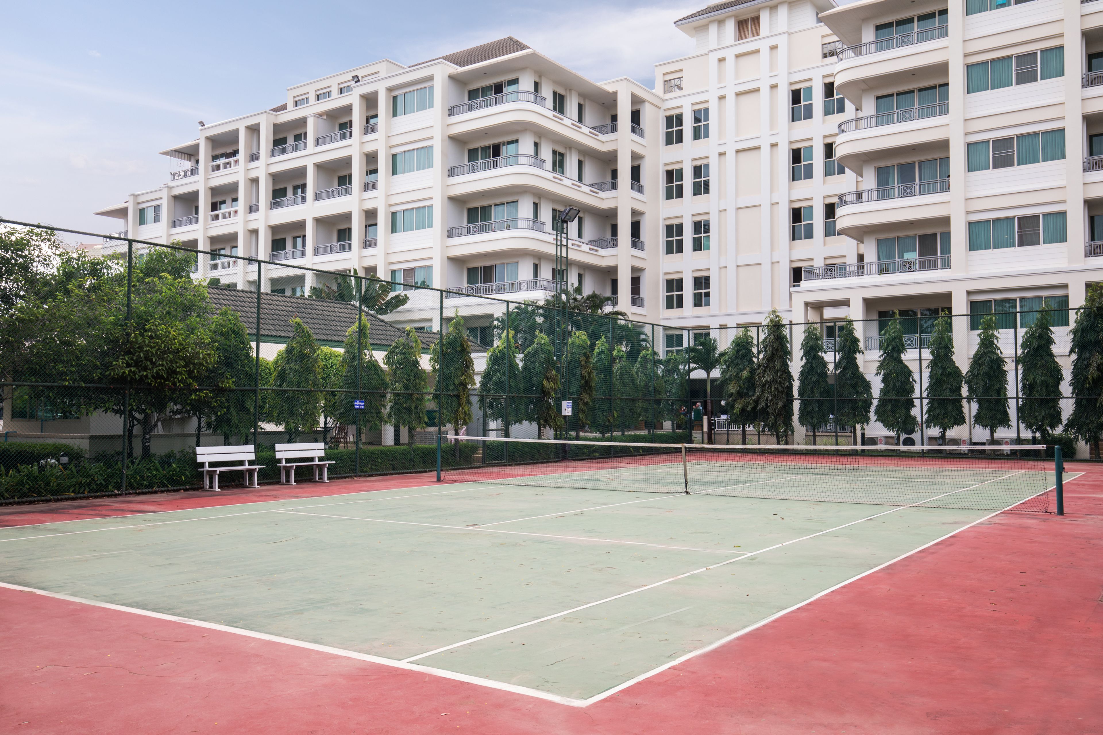 A tennis court with a net, surrounded by a fence and benches.