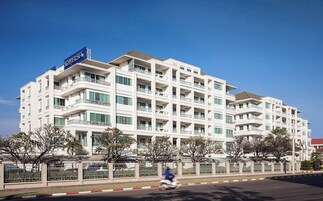 A multi-story hotel with balconies, a clear blue sky, and a street in front.