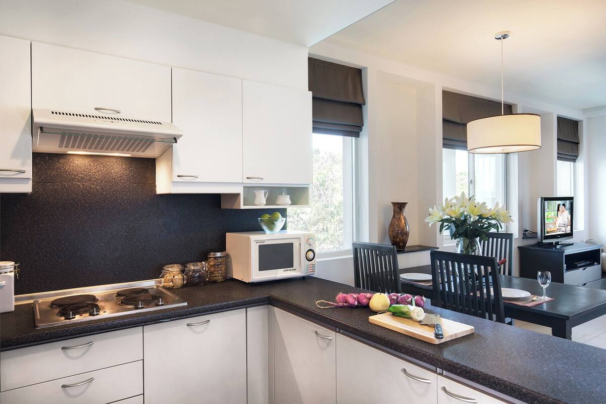 A modern kitchen with white cabinets, a black countertop, a microwave, and a dining area with a table and chairs.