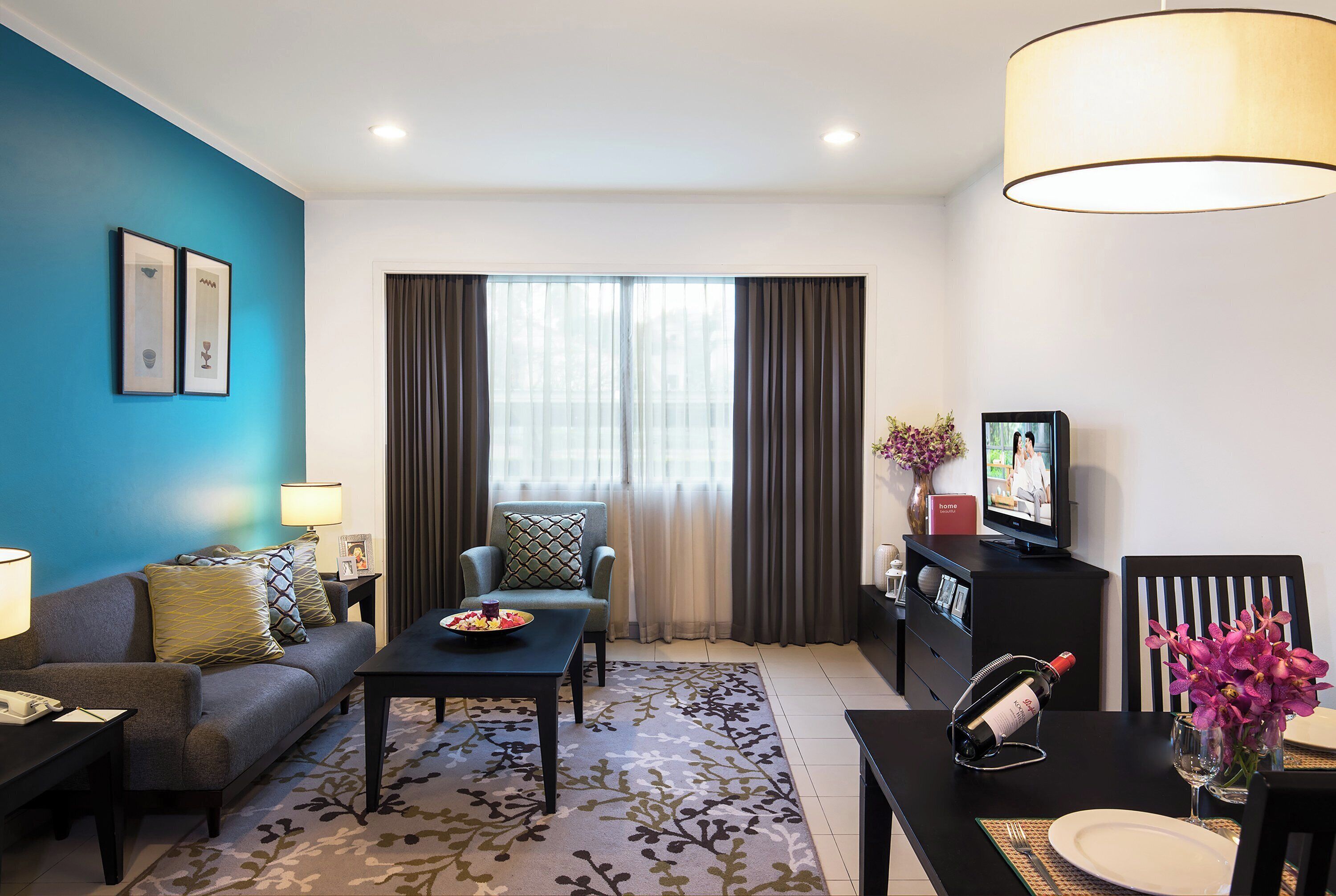 A modern living room with a sofa, coffee table, and TV. There is a dining area with a table and chairs.