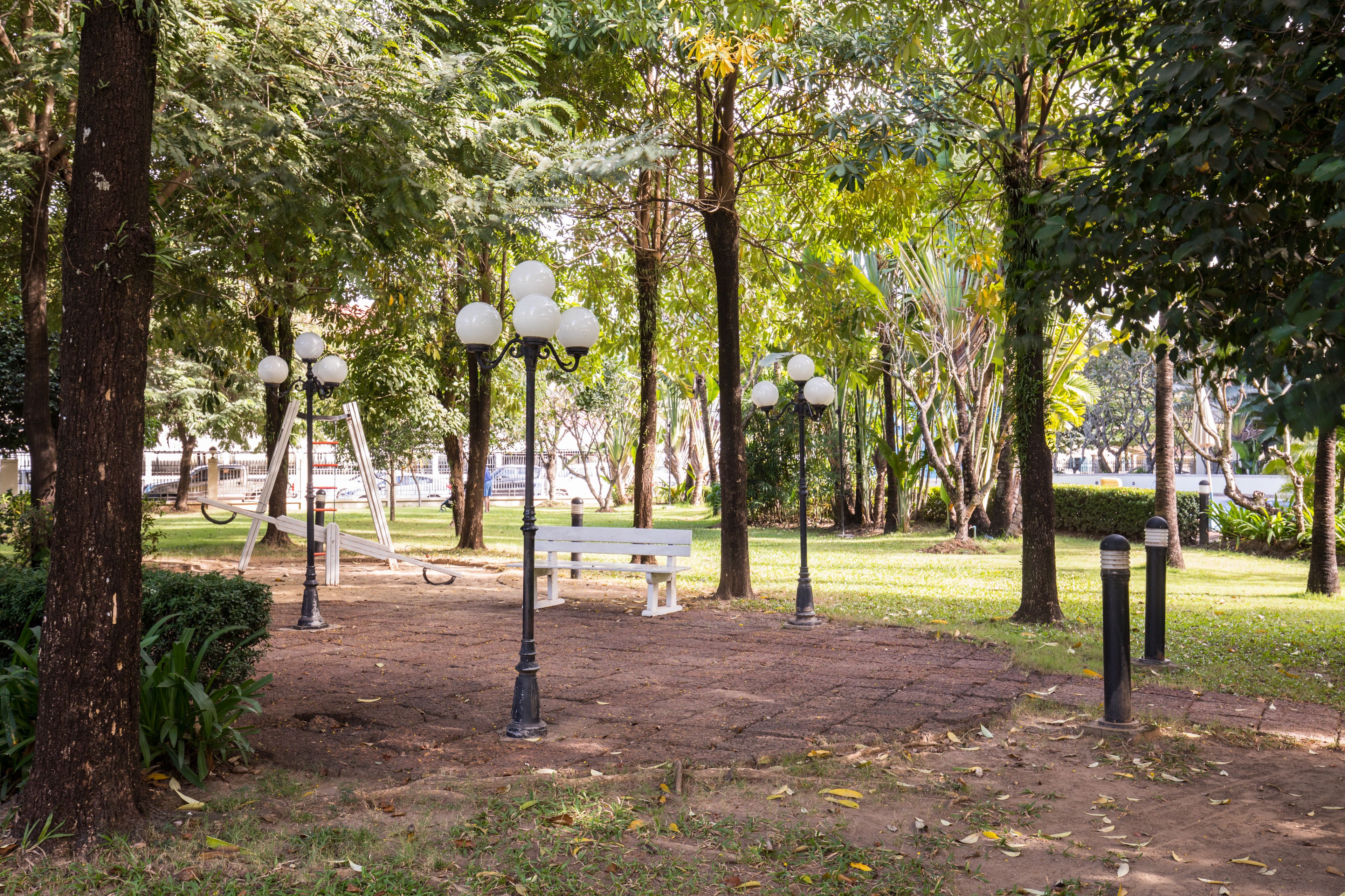 Un parque con un banco blanco, farolas y árboles.
