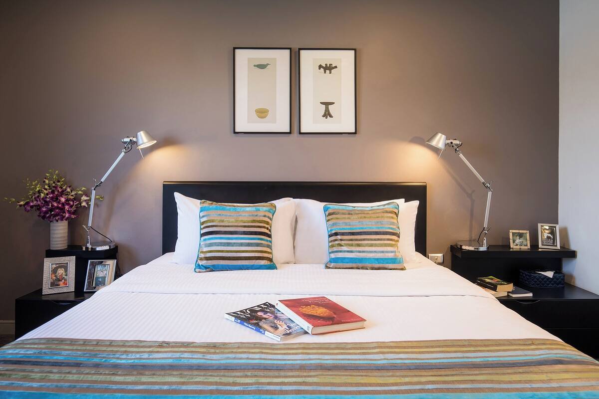 A neatly made bed with striped bedding, two bedside lamps, and framed artwork on the wall.