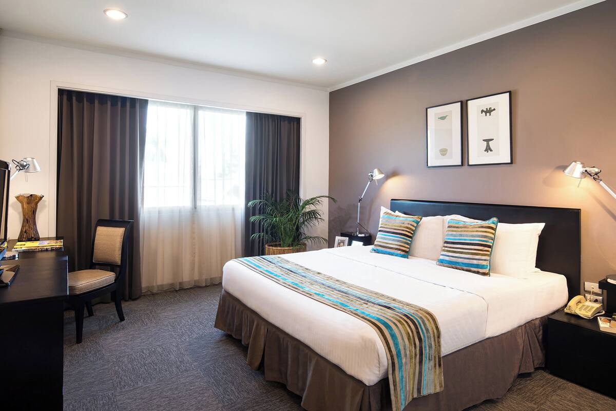 A hotel room with a large bed, a desk, a chair, and a potted plant.