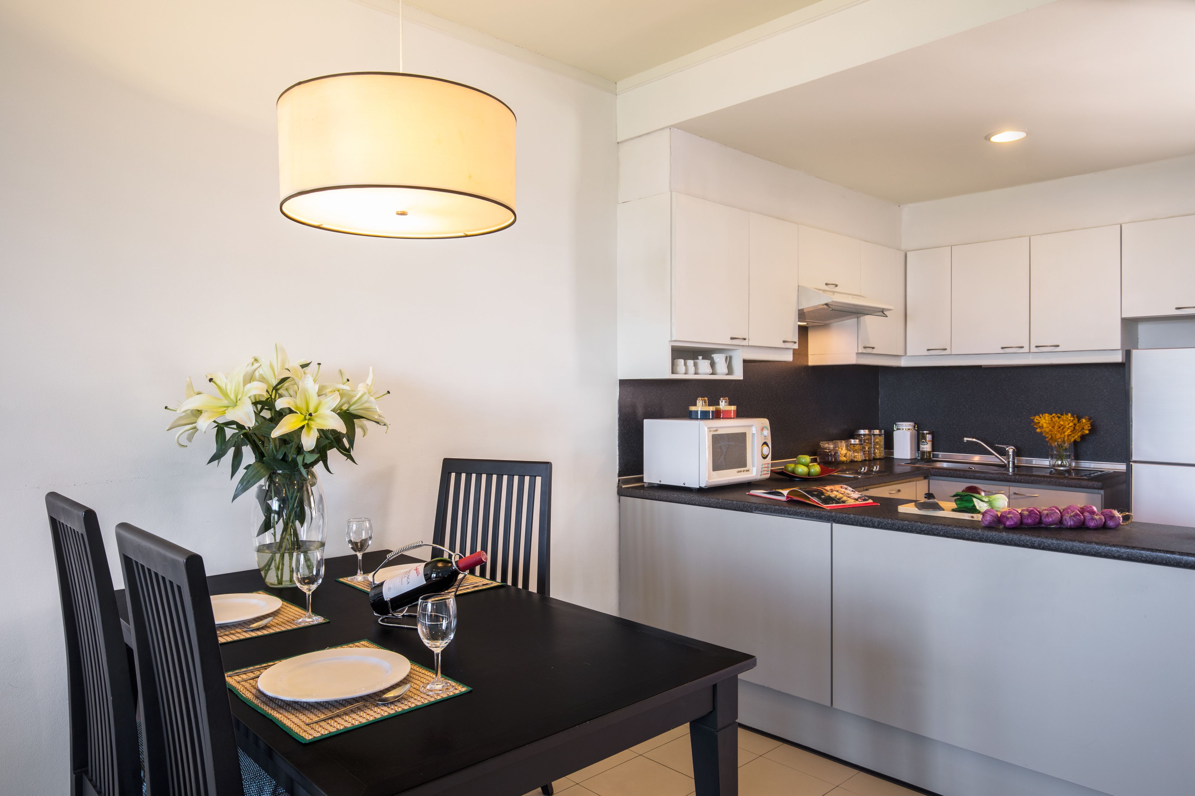A modern kitchen with white cabinets, a microwave, and a dining area with a table set for two.