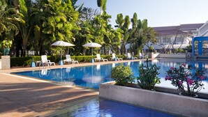 A pool area with lounge chairs and umbrellas, surrounded by lush greenery and a building in the background. - Somerset Vientiane (Vientiane)