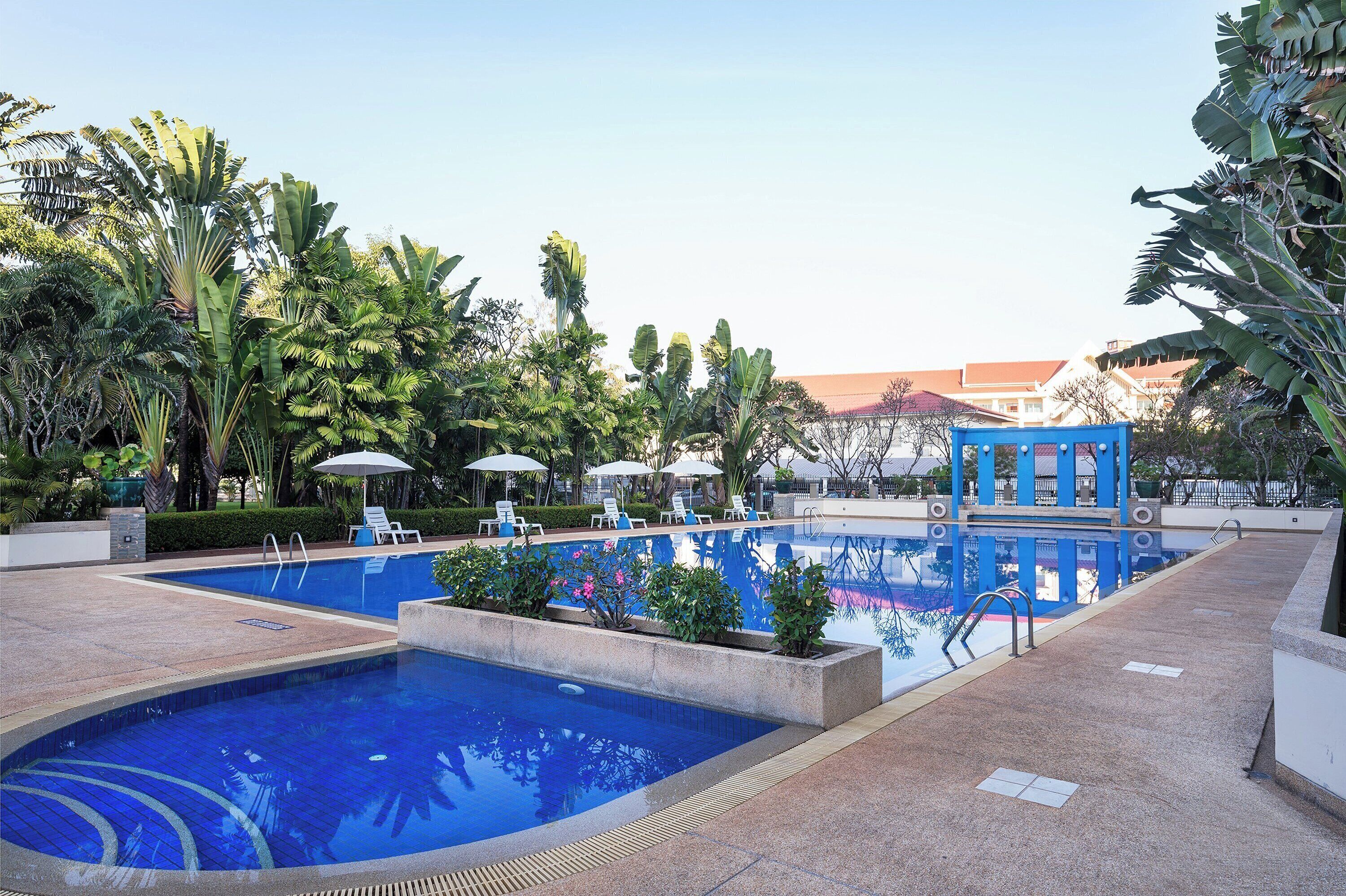 A swimming pool with two sections, surrounded by lush greenery and lounge chairs.