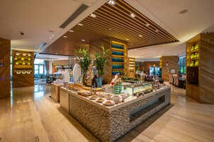 Una hall d'hotel moderna con un'area buffet centrale, pannelli in legno a soffitto e un pavimento pulito e lucido.