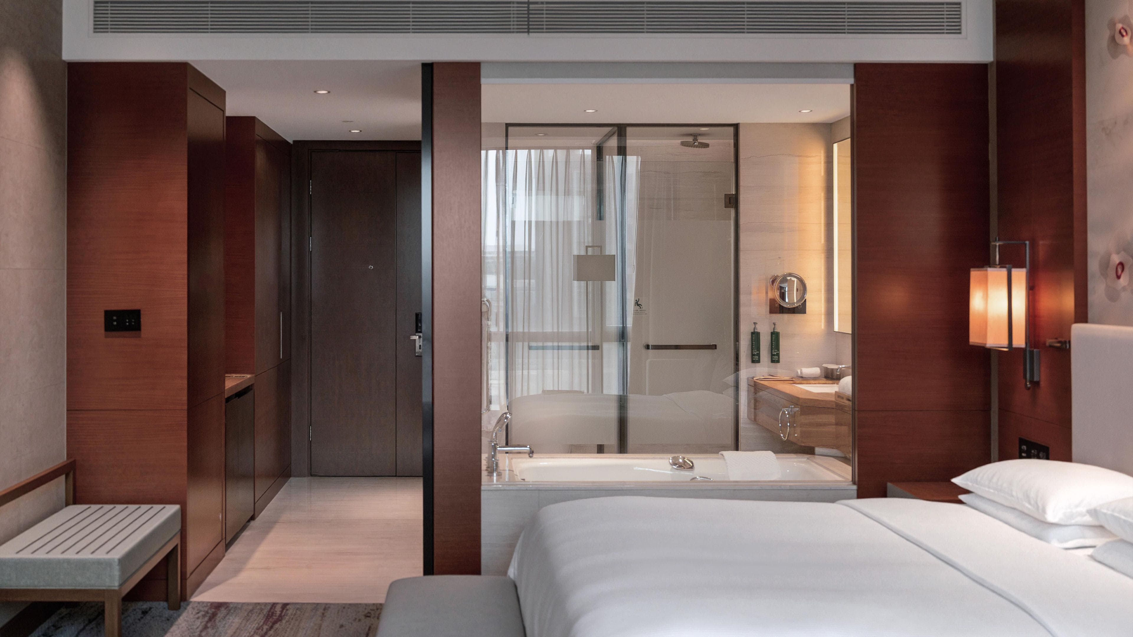 A modern hotel room with a large bed, a separate shower area, and a walk-in closet.
