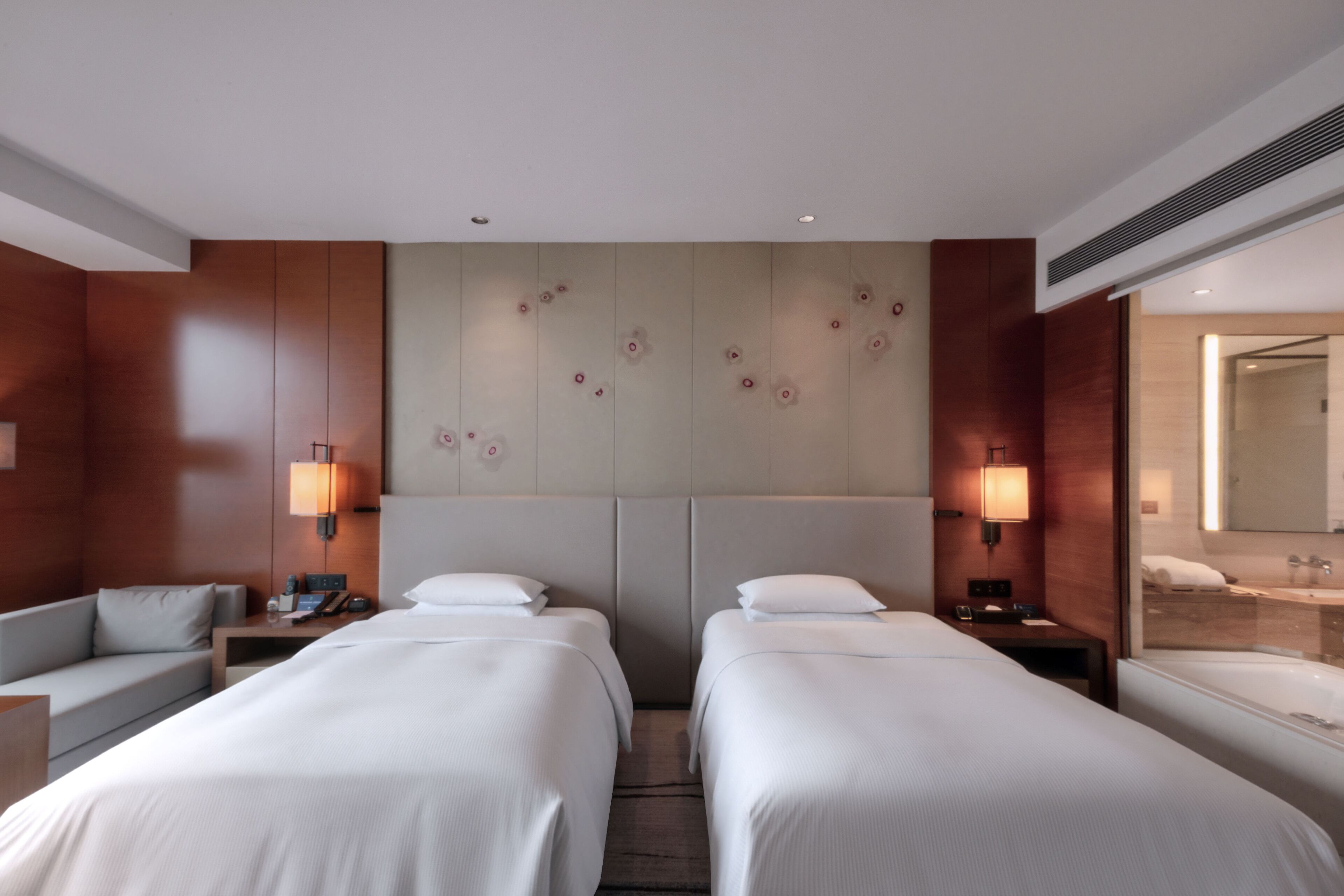 Een hotelkamer met twee bedden, een bank, een bureau en een badkamer met een grote spiegel.