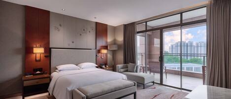 A modern hotel room with a large bed, a desk, a chair, and a balcony with a city view.