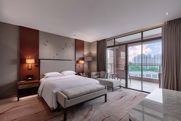 A modern hotel room with a large bed, a desk, a chair, and a balcony with a city view.