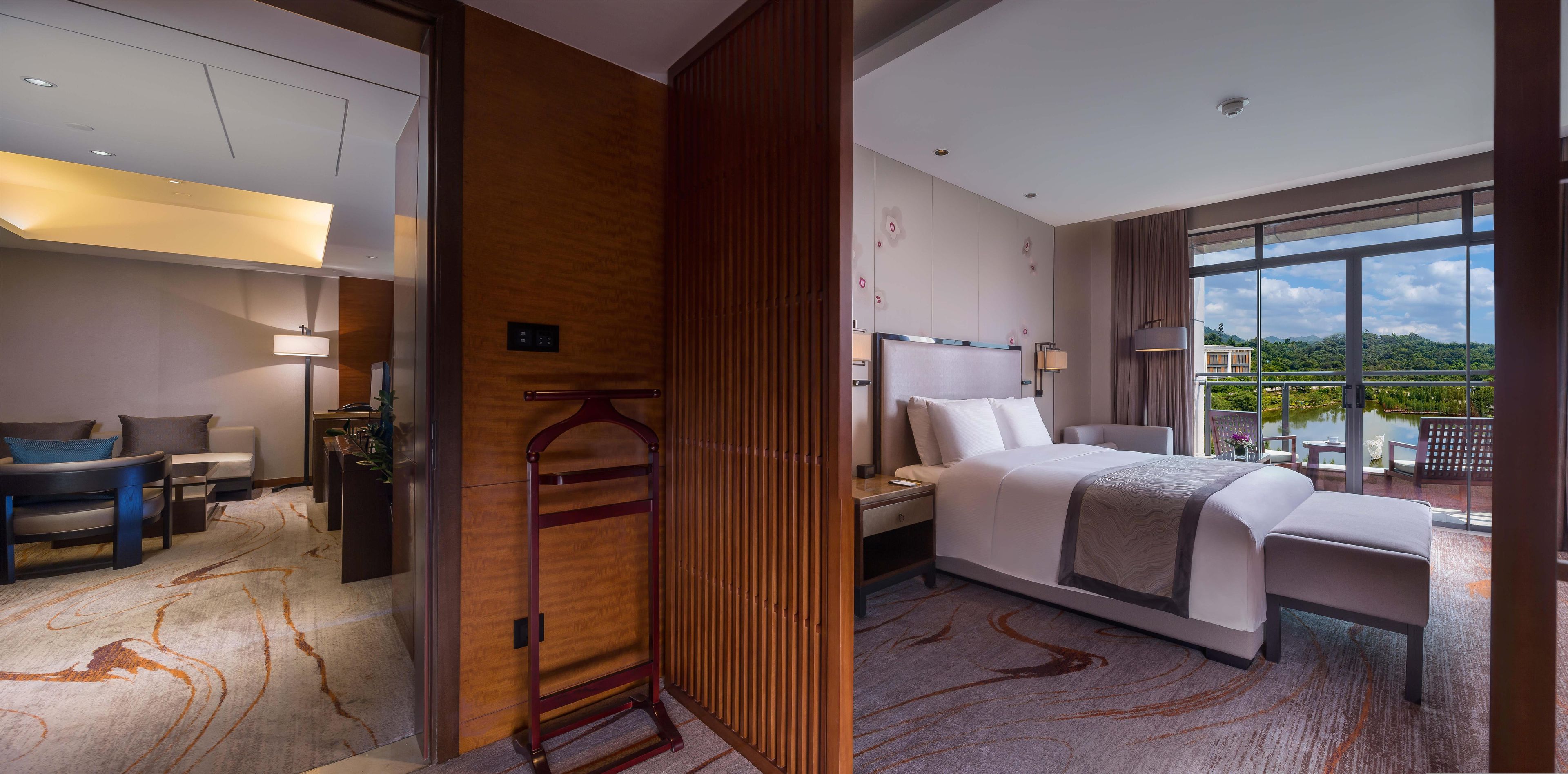 Habitación de hotel con cama, mesita de noche, lámpara y vistas a un lago.