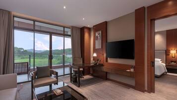 Une chambre d’hôtel moderne dotée d’un grand balcon, d’une télévision à écran plat, d’un bureau avec une lampe et d’un coin salon confortable.