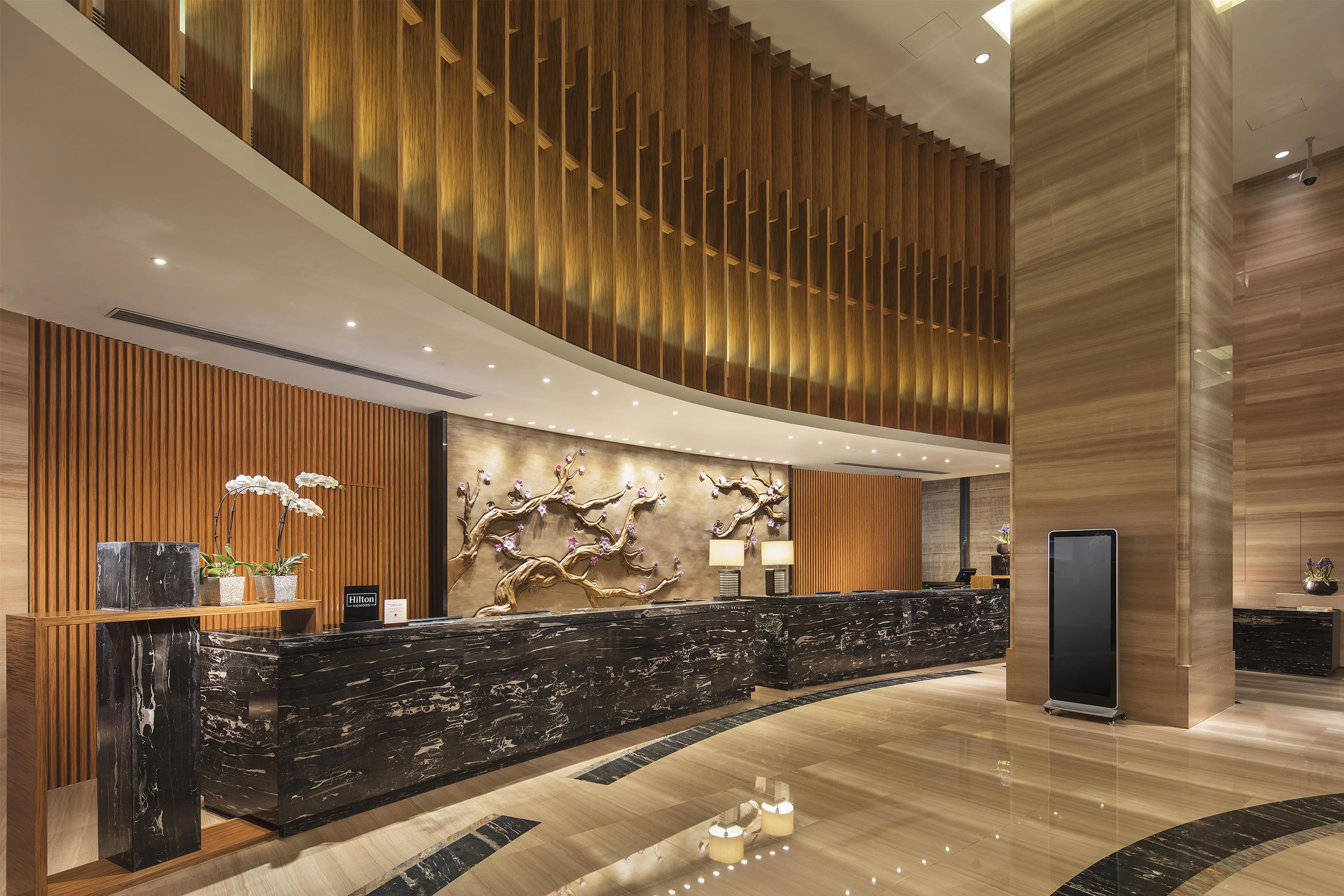 A hotel reception area with a curved marble counter, wooden paneling, and a wall-mounted floral sculpture.