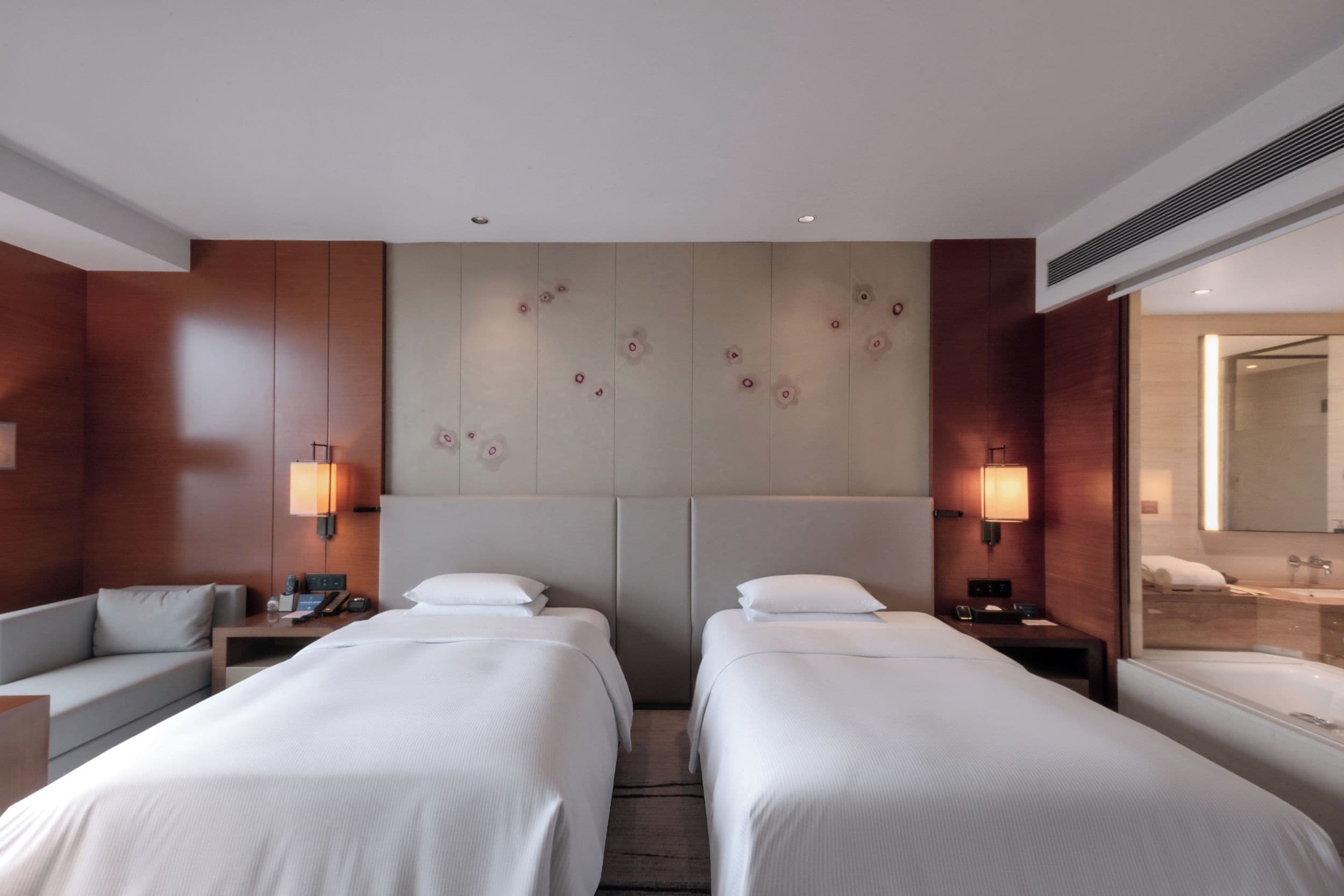 A hotel room with two beds, a sofa, a desk, and a bathroom with a mirror and sink.