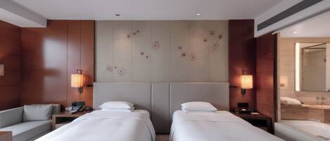 A hotel room with two beds, a sofa, a desk, and a bathroom with a mirror and sink.