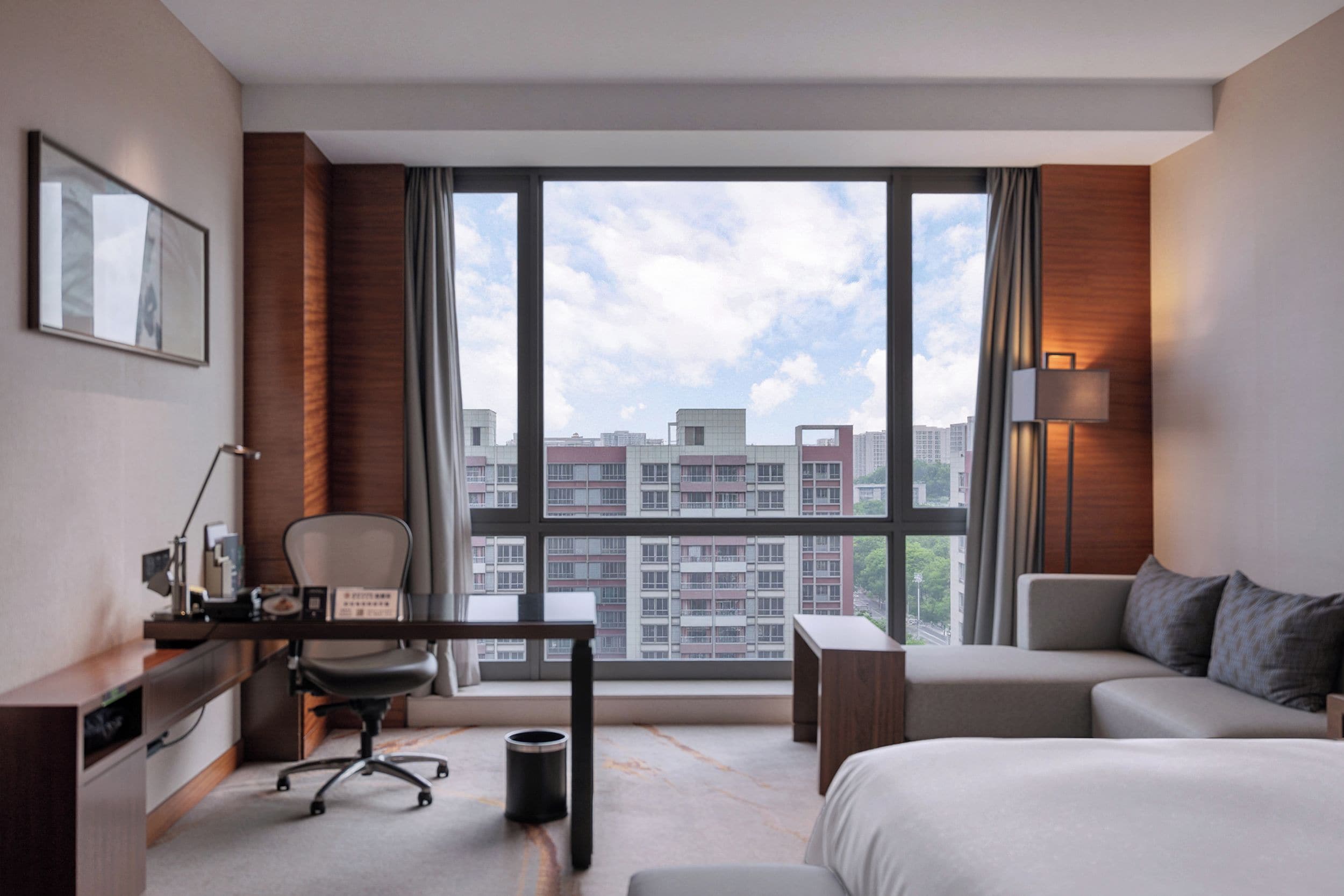 Una habitación de hotel moderna con un ventanal grande, un escritorio, una silla, un sofá y una cama.
