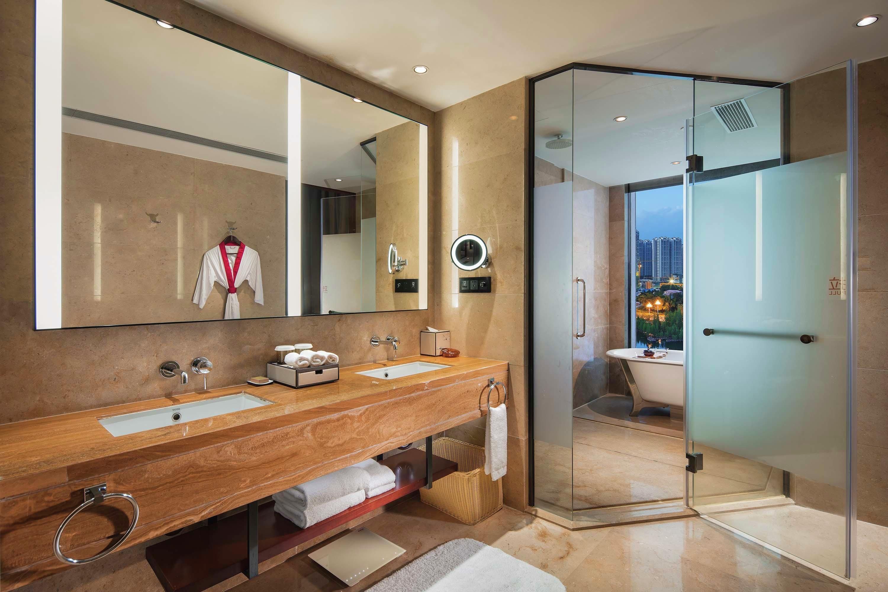 Een moderne badkamer met een wastafel met dubbele wastafel, een grote spiegel, een douchecabine van glas en uitzicht op een stadsgezicht.