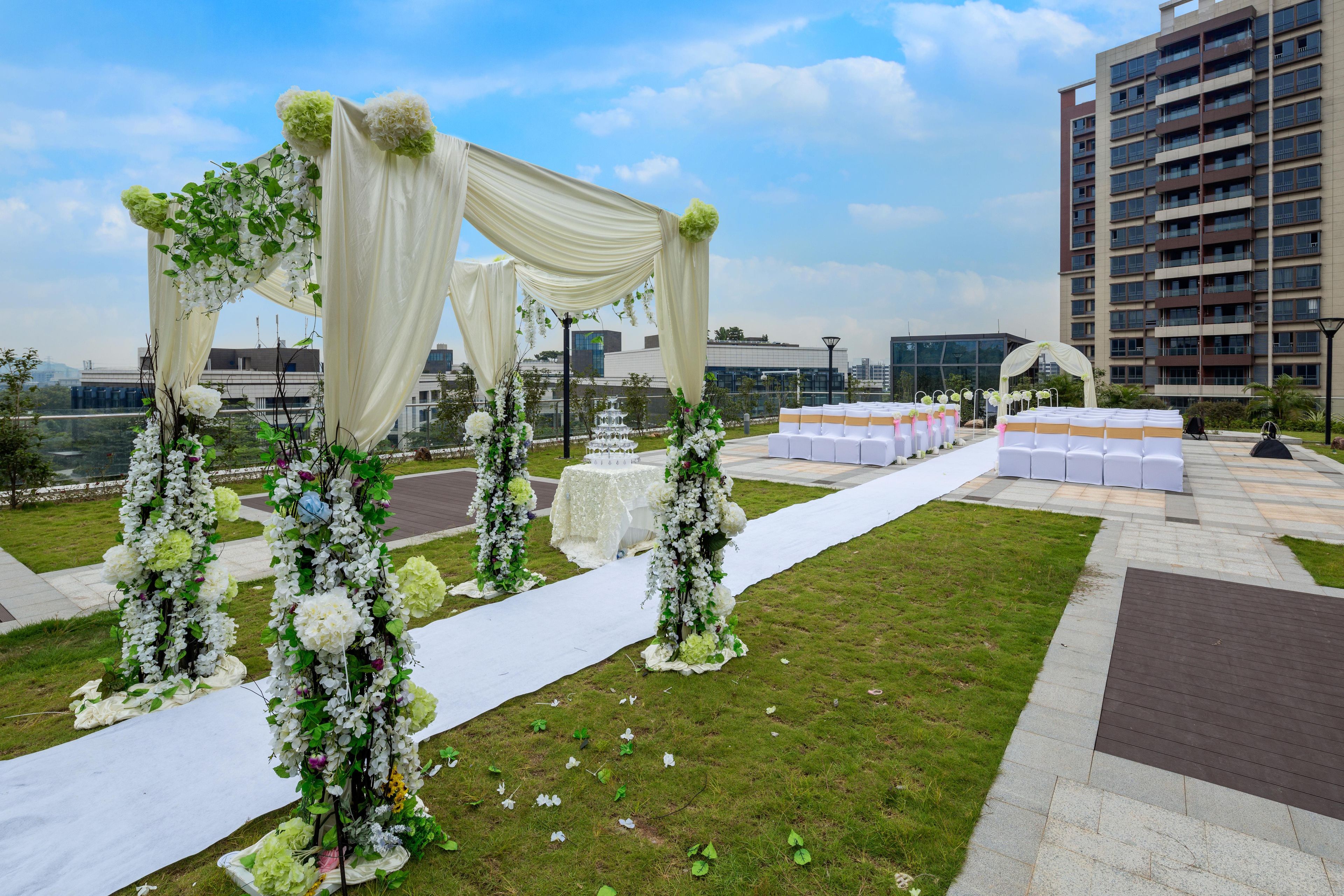 Eine Hochzeit im Freien mit einem weiß drapierten Torbogen, Blumenarrangements und einer Sitzgelegenheit.