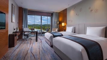 Ett hotellrum med två sängar, ett skrivbord, en stol, en TV och ett stort fönster med utsikt.