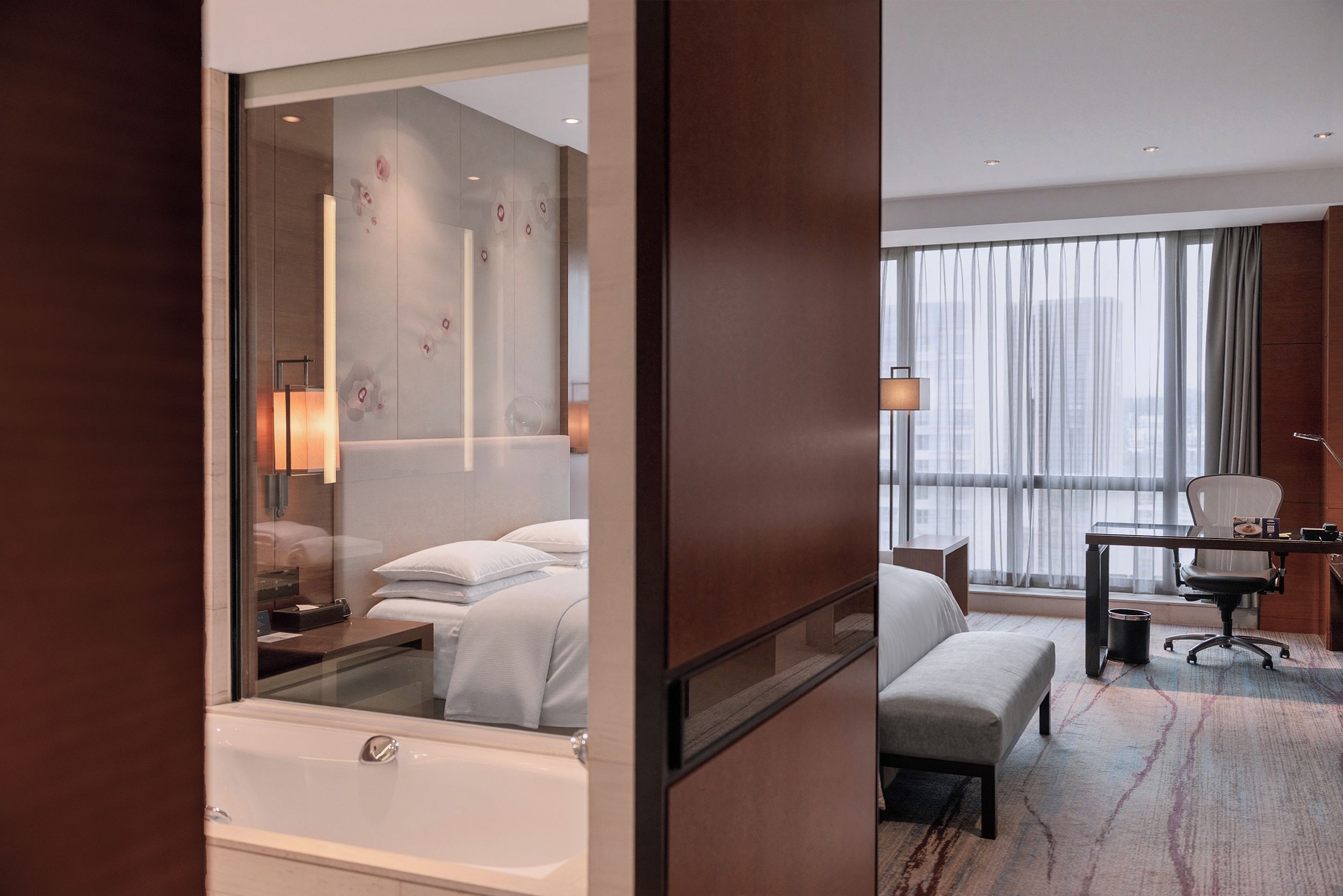 Une chambre d’hôtel moderne dotée d’une grande fenêtre, d’un bureau, d’une chaise, d’un banc et d’une baignoire.