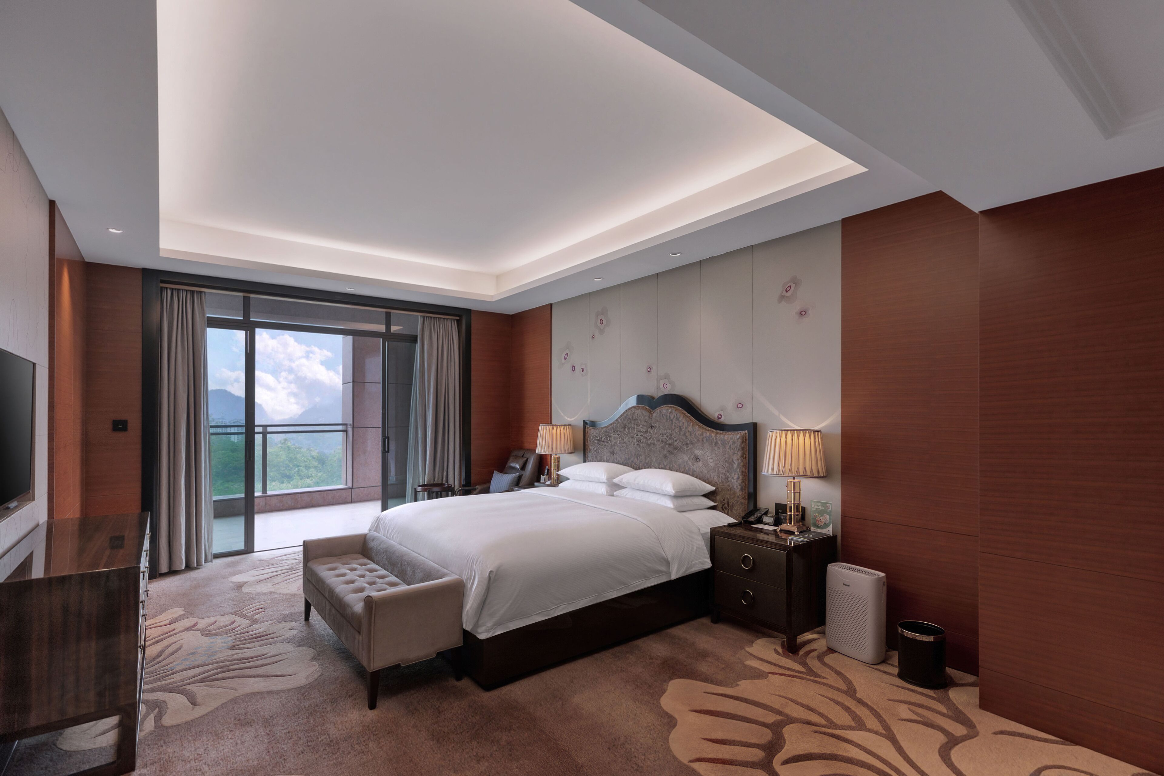 A modern hotel room with a large bed, a desk, a TV, and a view of the outdoors.