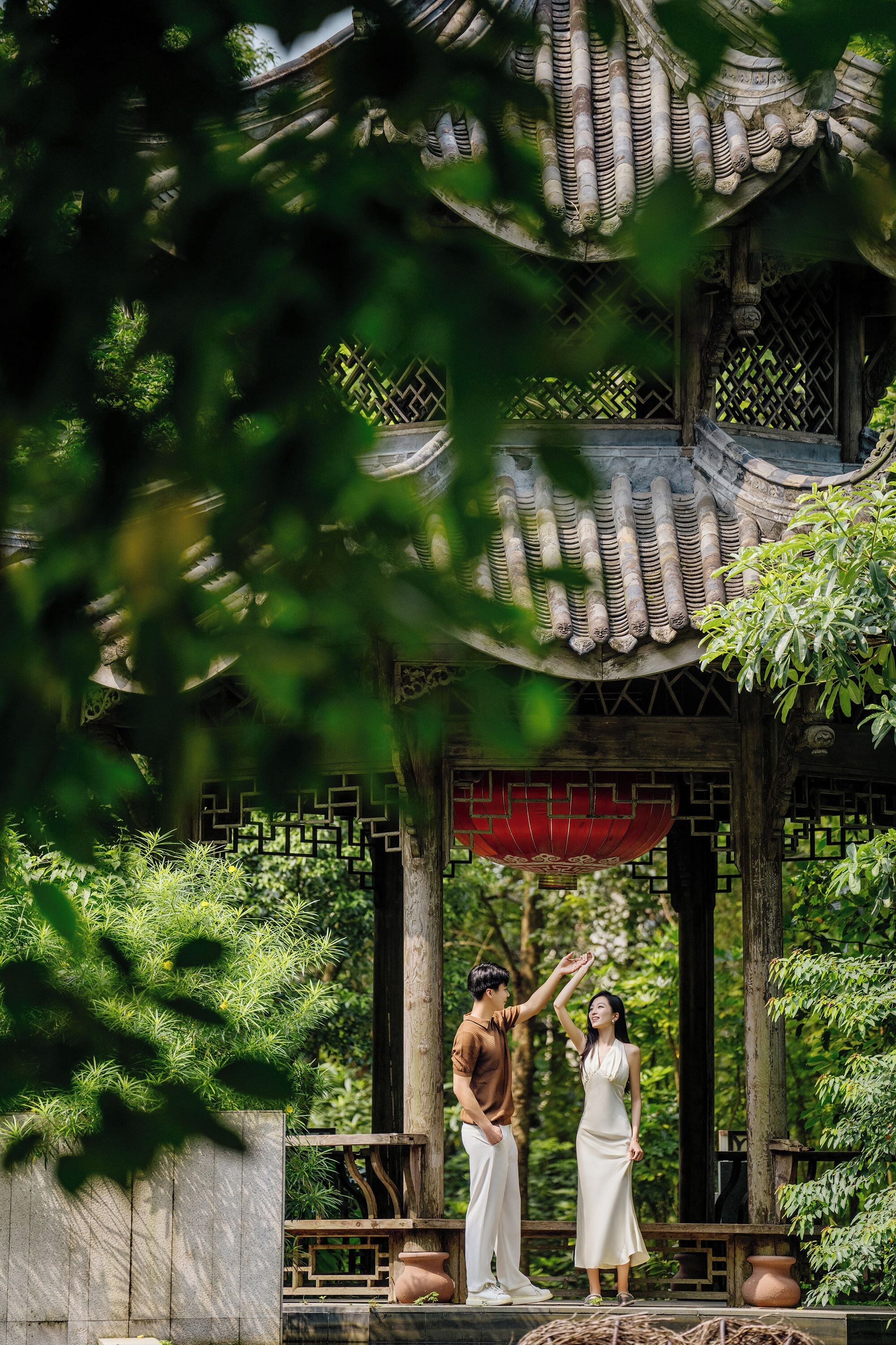 A traditional pavilion with a tiled roof and wooden pillars, surrounded by lush greenery.