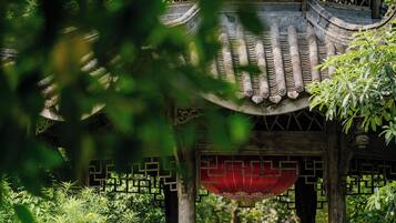 A traditional pavilion with a tiled roof and wooden pillars, surrounded by lush greenery.