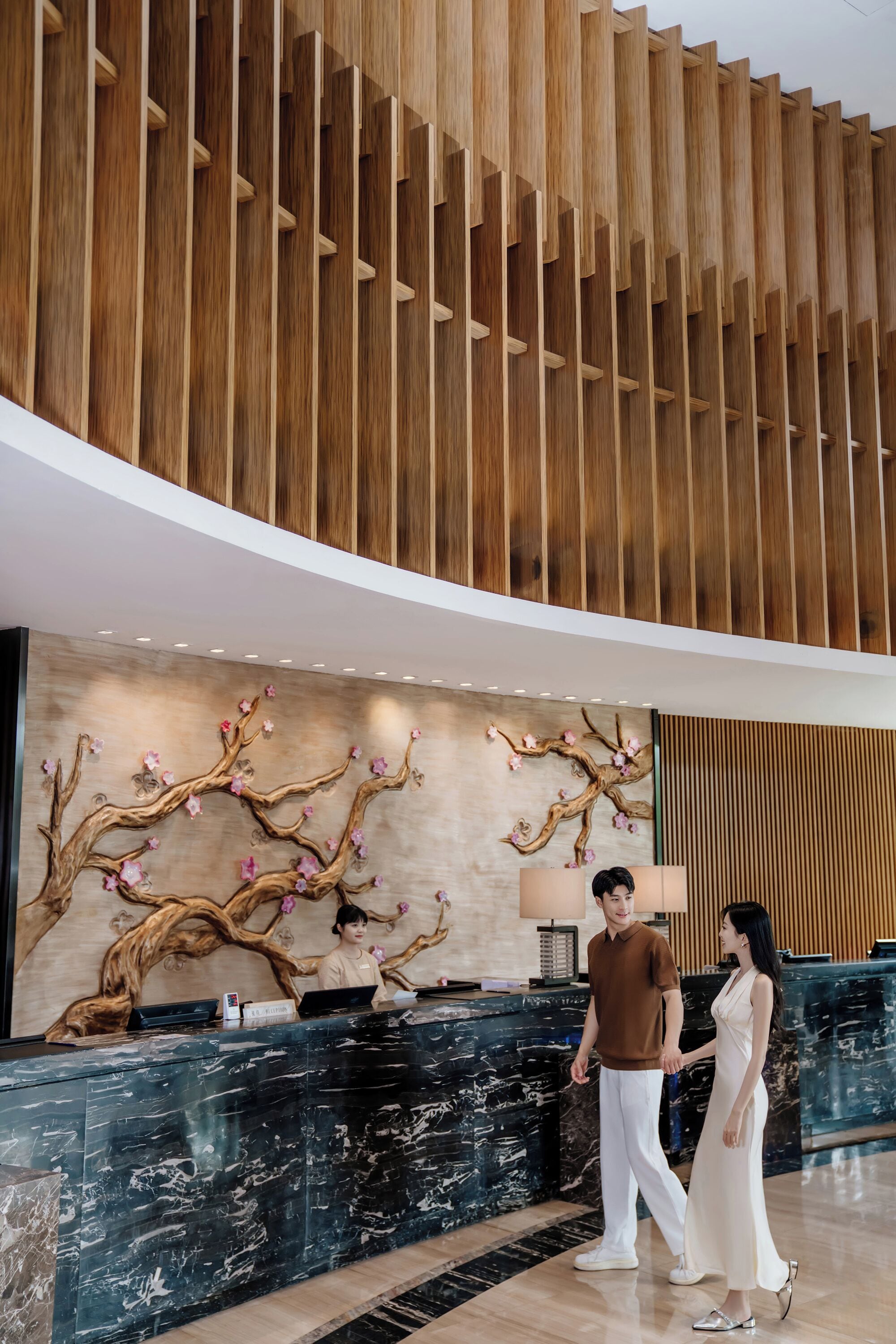 A reception area with a wooden ceiling, a marble reception desk, and a wall with a tree branch design.