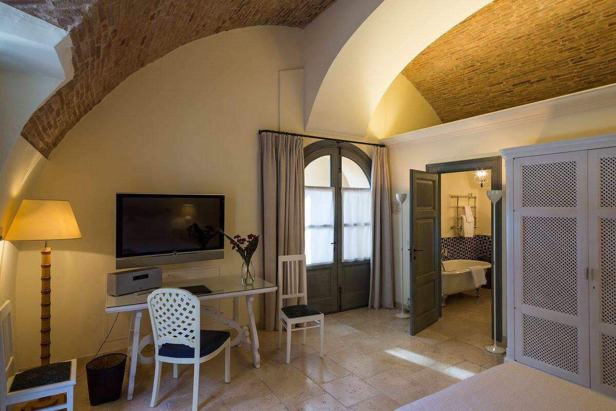 A room with a TV, a desk, a chair, a lamp, and a view of a bathroom.
