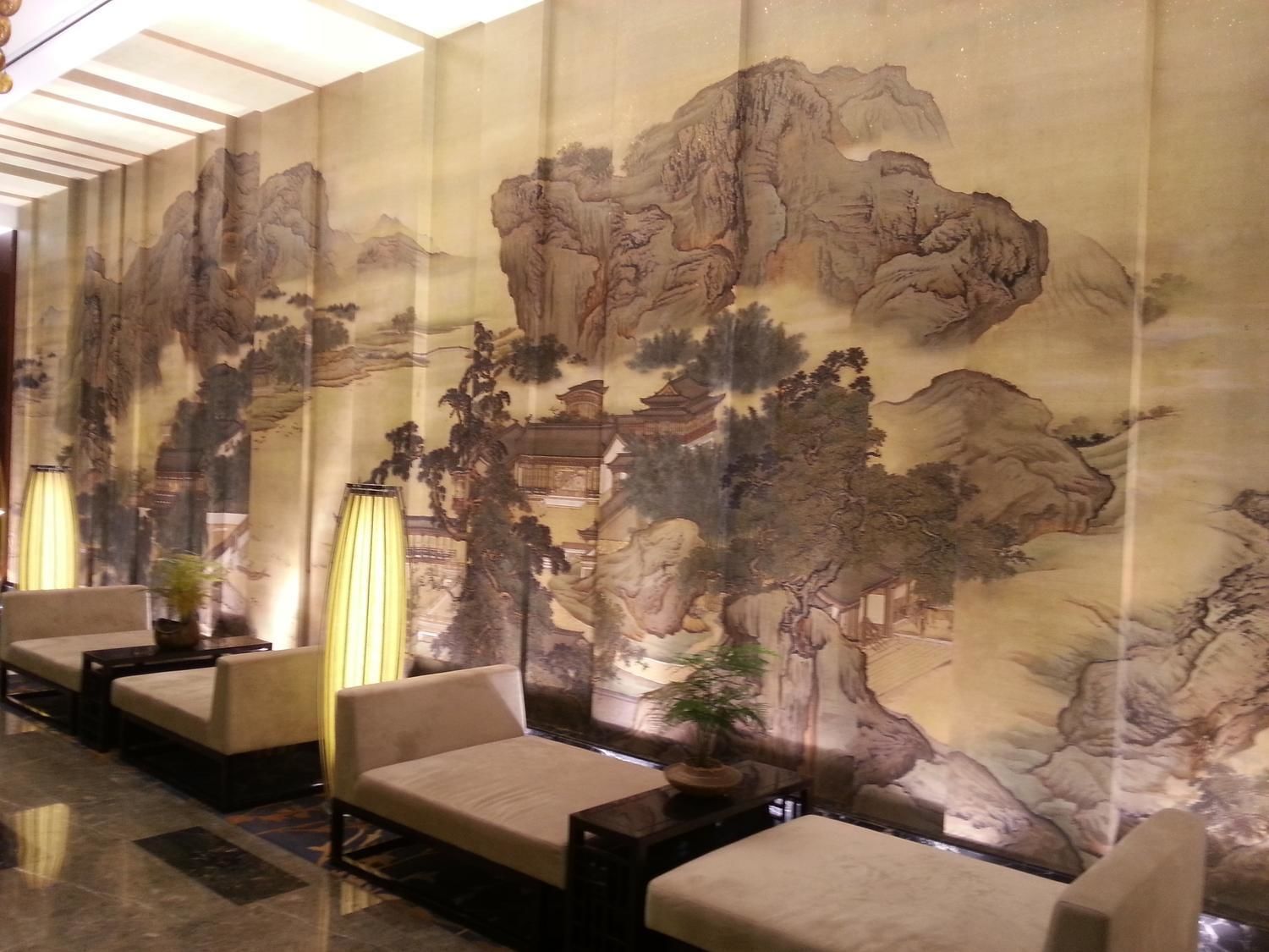 A lobby with traditional Chinese-style wall art, seating areas, and a modern floor design.