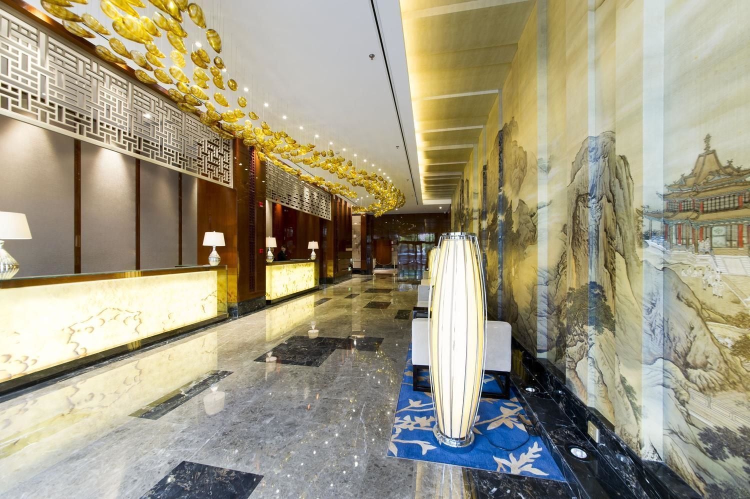 En hotellobby med en receptionsdisk, en dekorativ vägg med en väggmålning och ett mönstrat golv.