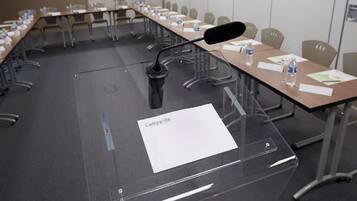 Een vergaderzaal met een lange tafel, stoelen en een microfoon.