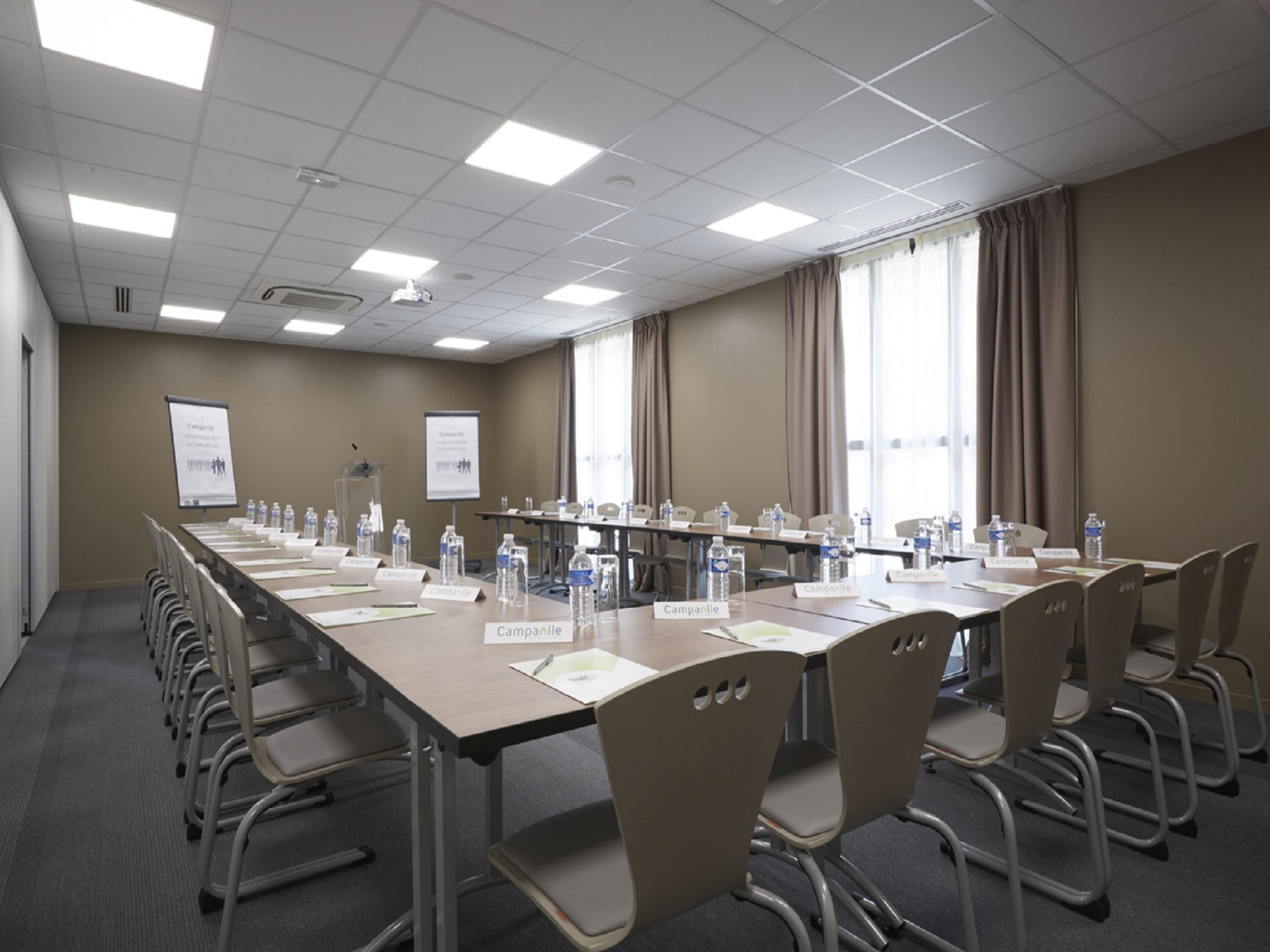 A conference room with a long table, chairs, nameplates, water bottles, and presentation screens.
