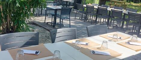 An outdoor dining area with tables and chairs, surrounded by greenery.