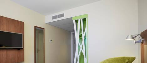 A hotel room with a bed, a television mounted on the wall, a door, and a green partition.