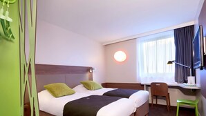 Habitación de hotel con dos camas, un escritorio, una silla, un televisor y una ventana con cortinas.