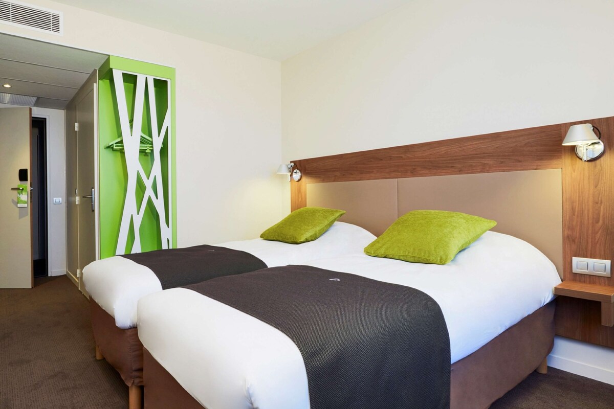 A hotel room with two beds, a green accent wall, and a wooden headboard.