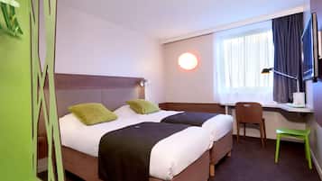Ein Hotelzimmer mit zwei Betten, einem Schreibtisch, einem Stuhl, einem Fernseher und einem Fenster mit Vorhängen.