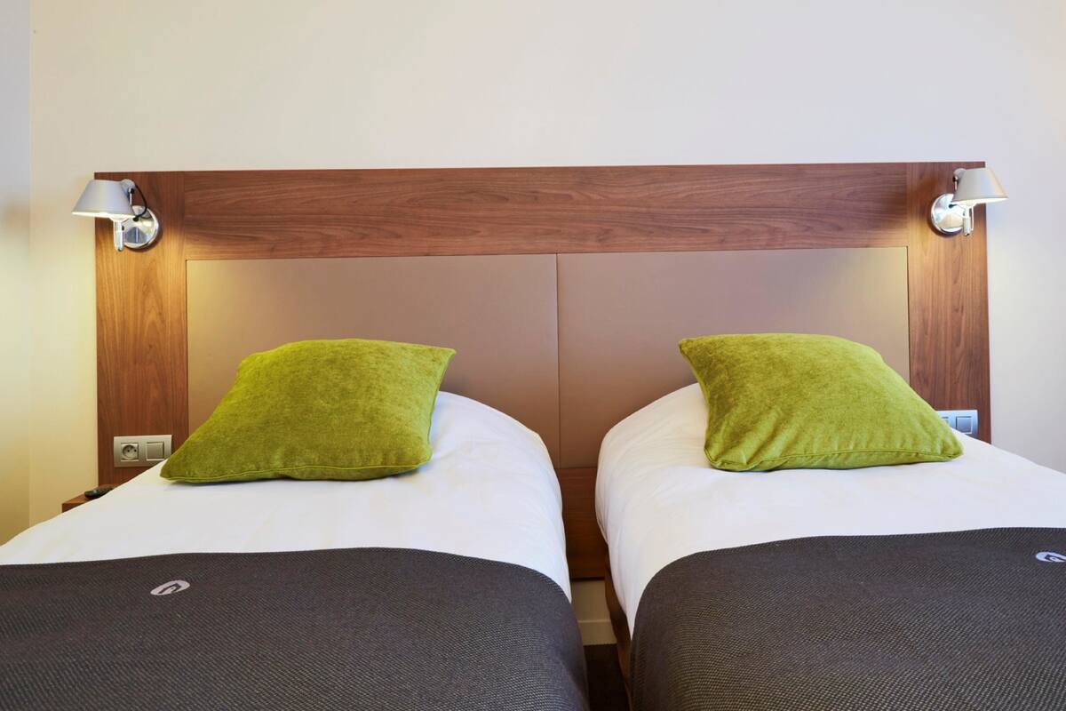 Une chambre d’hôtel avec deux lits, chacun agrémenté d’un oreiller vert et d’une couvre-lit de couleur foncée.