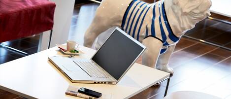 Una estatua de un bulldog usando una camisa a rayas, una computadora portátil, un teléfono inteligente, una taza y una cuchara sobre una mesa en un ambiente interior moderno.